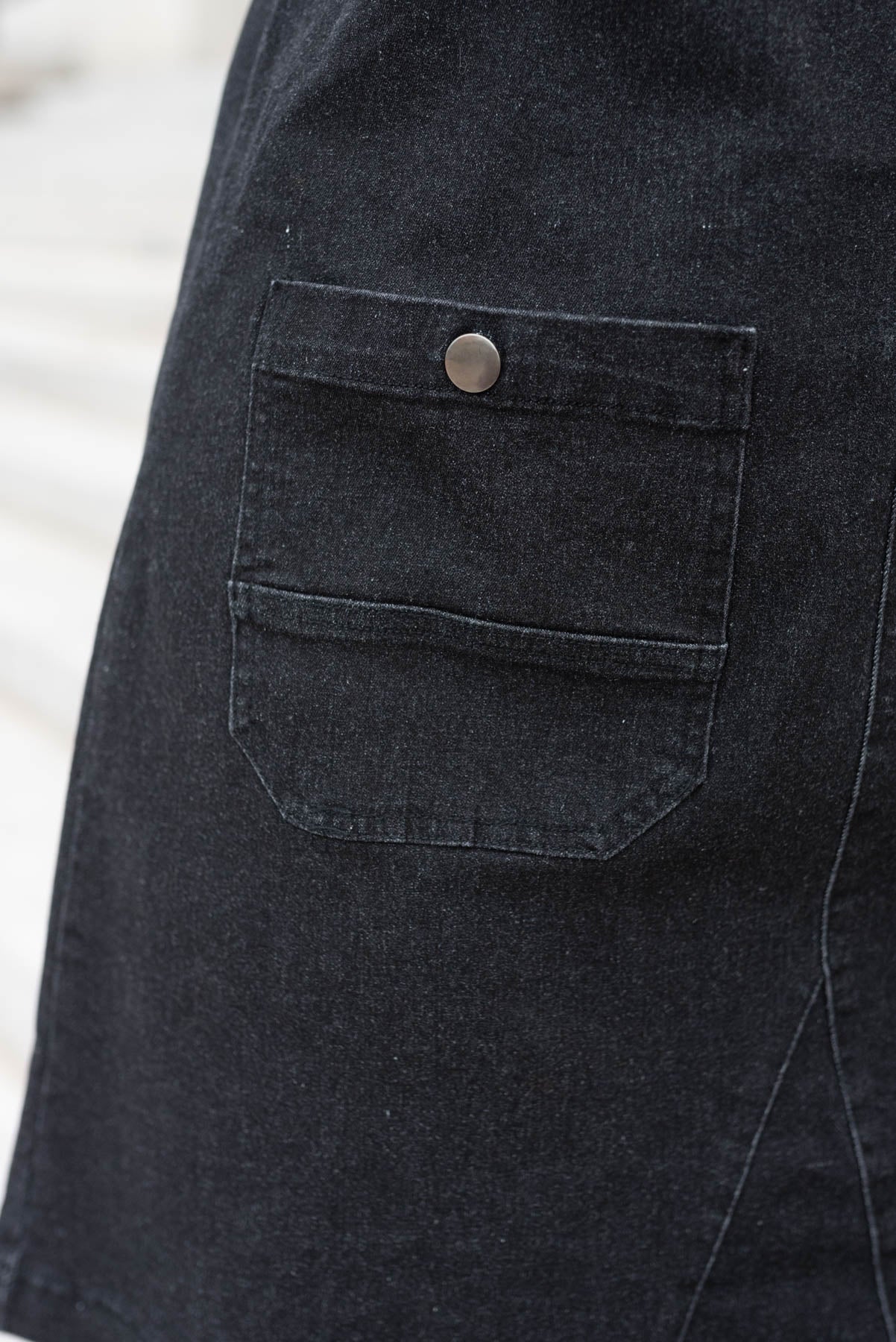 Close up of the front pockets on the black denim overall dress