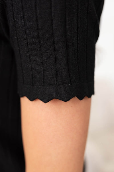 Close up of the sleeve and scalloped cuff on the black button top