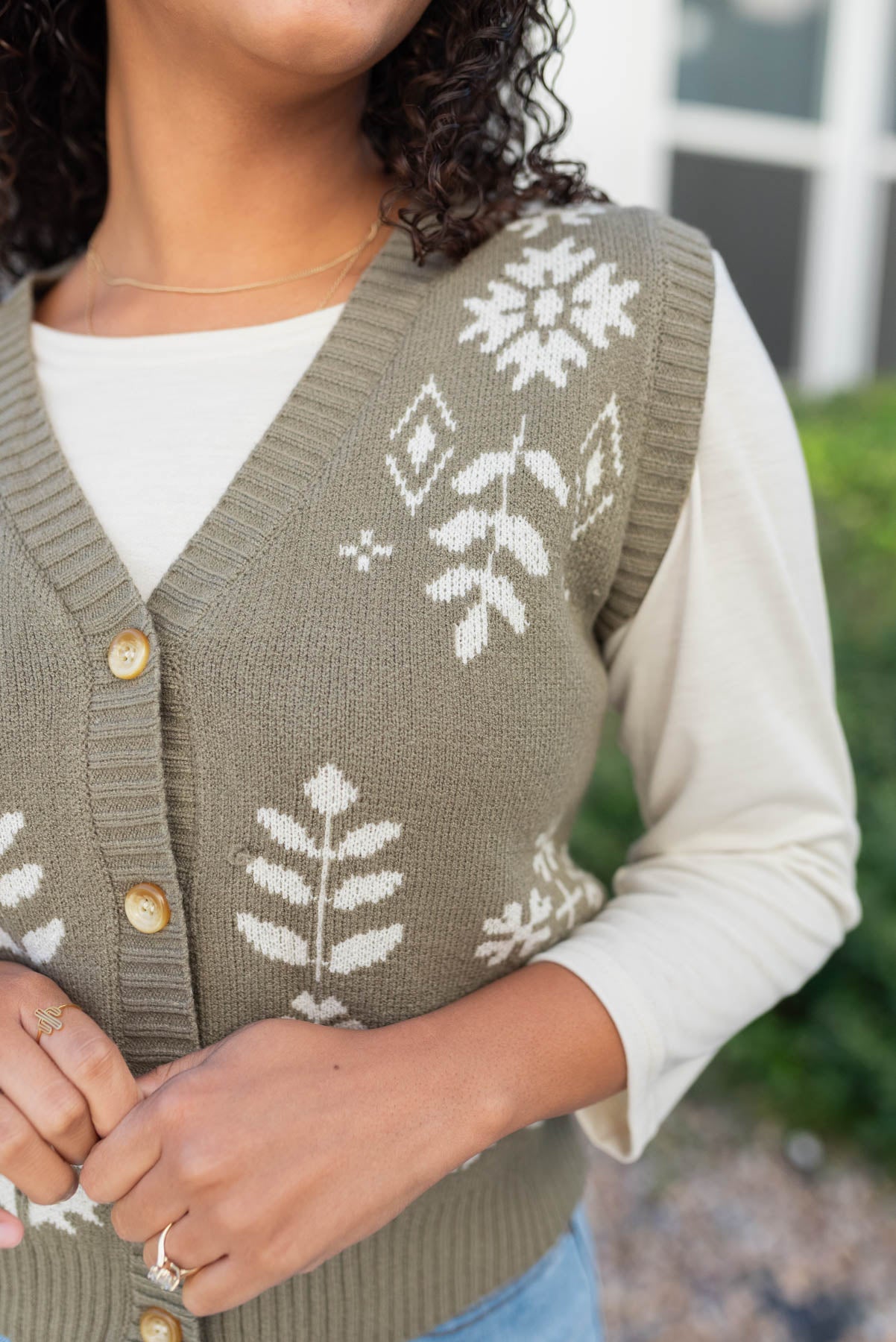 Close up of the ivory pattern on the light olive floral sweater vest